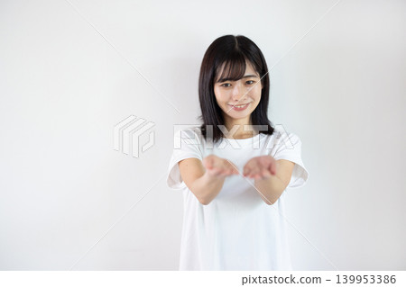 A young Japanese woman smiles, extending her palm in front of a white background. A young Japanese woman smiles, extending her palm in front of a white background. 139953386