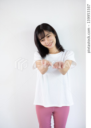 A young Japanese woman smiles, extending her palm in front of a white background. A young Japanese woman smiles, extending her palm in front of a white background. 139953387