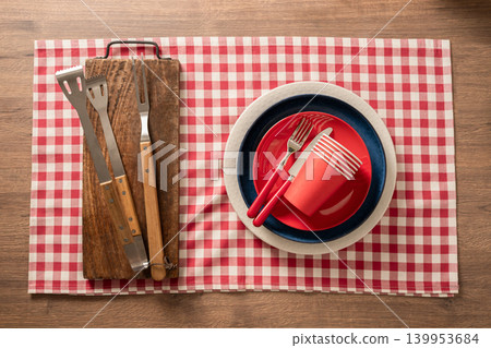 BBQ tools on wooden board and red checkered tablecloth picnic setup 139953684