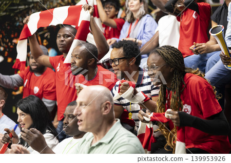 Female soccer fans celebrating goal with raised arms in crowded stadium stands, red team supporters and energetic live match atmosphere in fan section. Supporters remain nervous. Female soccer fans celebrating goal with raised arms in crowded stadium stands, red team supporters and energetic live match atmosphere in fan section. Supporters remain nervous. 139953926