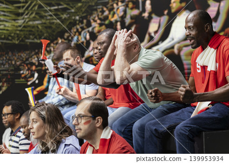 Frustrated football supporters gesturing with open hands in stadium stands, reacting to tense live soccer match moment and close call. Anxious crowd show suspense, last minute pressure. 139953934