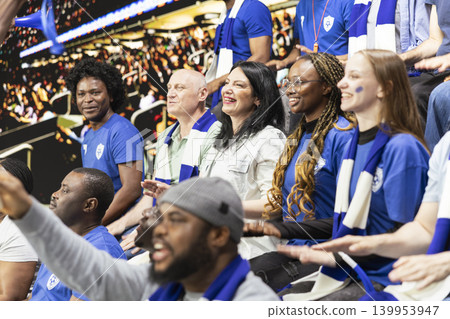 Diverse blue team women supporters cheering loudly with raised arms in packed stadium stands during exciting live soccer match. Team spirit and celebration inside the stadium terrace. Diverse blue team women supporters cheering loudly with raised arms in packed stadium stands during exciting live soccer match. Team spirit and celebration inside the stadium terrace. 139953947