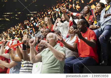 Ecstatic football supporters cheering and waving scarves after dramatic goal during live soccer match in crowded stadium stands. Joyful crowd reaction, raised fists and jumping fans. Ecstatic football supporters cheering and waving scarves after dramatic goal during live soccer match in crowded stadium stands. Joyful crowd reaction, raised fists and jumping fans. 139953950
