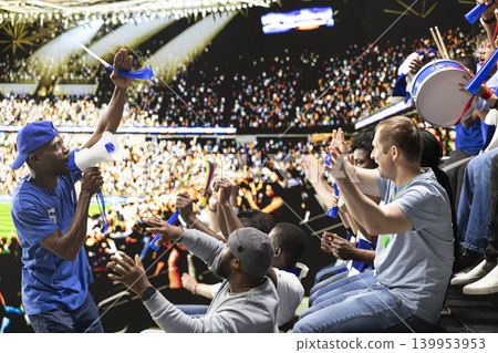 Blue team football capo standing above crowd with megaphone, leading passionate supporter section during energetic stadium chant. Organized fans producing powerful support chants. Blue team football capo standing above crowd with megaphone, leading passionate supporter section during energetic stadium chant. Organized fans producing powerful support chants. 139953953