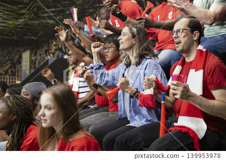 Packed stadium crowd of red team football supporters cheering with red horns and scarves during thrilling live soccer match. Emotional crowd reactions and fan chants, equality in football. Packed stadium crowd of red team football supporters cheering with red horns and scarves during thrilling live soccer match. Emotional crowd reactions and fan chants, equality in football. 139953978