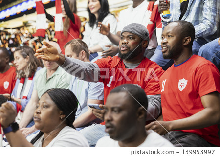 African american fans tracking live score for a bet ticket on mobile app, watching intense football match at the stadium. Supporters placing high risk wager on betting app, match update. African american fans tracking live score for a bet ticket on mobile app, watching intense football match at the stadium. Supporters placing high risk wager on betting app, match update. 139953997