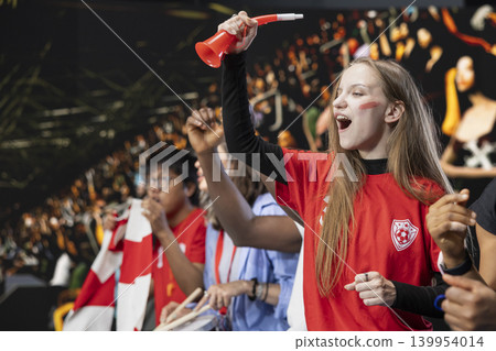Teenager football fan cheering for the winning team from stadium stands, girl with face paint jumping and screaming after national team wins the world championship. Raised fists and joy. Teenager football fan cheering for the winning team from stadium stands, girl with face paint jumping and screaming after national team wins the world championship. Raised fists and joy. 139954014