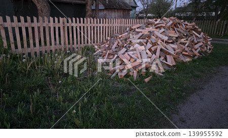 Pile of chopped firewood stacked near a wooden fence outdoors, rustic yard scene with logs for heating, storage and country life. Pile of chopped firewood stacked near a wooden fence outdoors, rustic yard scene with logs for heating, storage and country life. 139955592