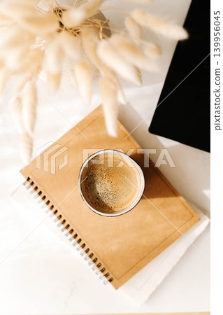 Minimal desk flat lay with coffee cup, notebook and laptop corner on a white table Minimal desk flat lay with coffee cup, notebook and laptop corner on a white table 139956045
