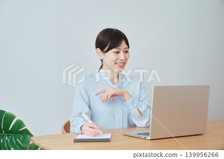 一位女士一邊上網工作一邊做筆記。 一位女士一邊上網工作一邊做筆記。 139956266