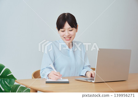 A woman working online while taking notes. 139956271