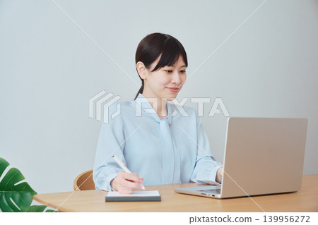 A woman working online while taking notes. 139956272