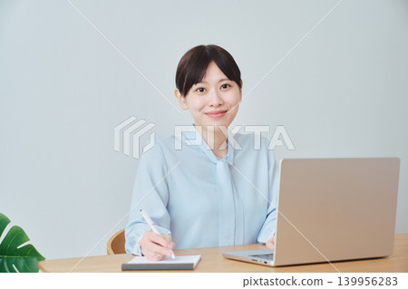 一位女士一邊上網工作一邊做筆記。 139956283