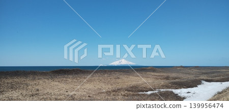 Mount Rishiri and the lingering snow of spring, seen in the distance across a sandy beach covered in withered grass. Mount Rishiri and the lingering snow of spring, seen in the distance across a sandy beach covered in withered grass. 139956474