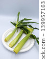 Three fresh, unhusked baby corn cobs are neatly arranged on a white plate. 139957163
