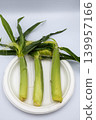 Three fresh, unhulled baby corn cobs lined up on a white plate (vertical overhead shot). 139957166