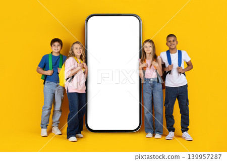 School children standing around large smartphone mockup on yellow studio background School children standing around large smartphone mockup on yellow studio background 139957287