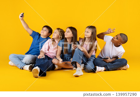 Diverse school children taking selfie together with smartphones on bright yellow background Diverse school children taking selfie together with smartphones on bright yellow background 139957290
