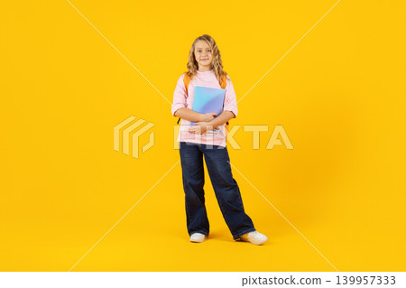 Schoolgirl with backpack holding notebook on yellow studio background, representing education 139957333