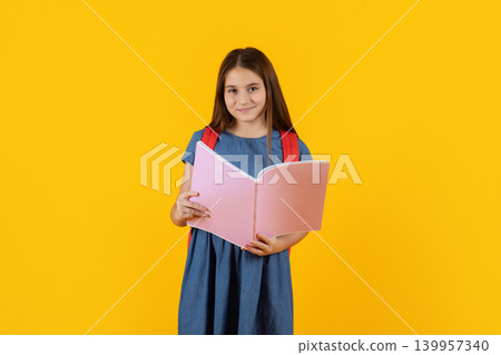 Smiling preteen schoolgirl reading colorful notebook on bright yellow studio background Smiling preteen schoolgirl reading colorful notebook on bright yellow studio background 139957340