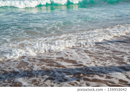 Sea waves wash over sandy beach with white foam and turquoise water during sunny summer vacation weather. Beach resort lifestyle coastal relaxation and seaside tourism Sea waves wash over sandy beach with white foam and turquoise water during sunny summer vacation weather. Beach resort lifestyle coastal relaxation and seaside tourism 139958042