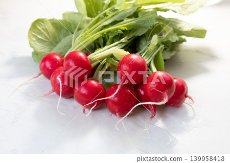 Fresh red radish with green leaves on marble table. Raw organic vegetable as source of fiber and vitamin. Healthy diet, vegan food and nutrition concept. Fresh harvest for cooking salad or raw snack. Fresh red radish with green leaves on marble table. Raw organic vegetable as source of fiber and vitamin. Healthy diet, vegan food and nutrition concept. Fresh harvest for cooking salad or raw snack. 139958418