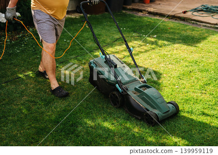 Person mowing lawn in backyard garden, home lawn care and summer yard maintenance Person mowing lawn in backyard garden, home lawn care and summer yard maintenance 139959119