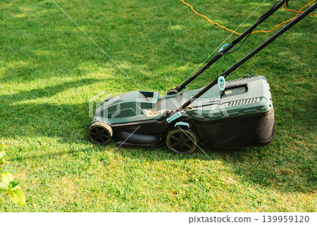 Electric lawn mower on green grass in backyard garden, lawn care and yard maintenance concept Electric lawn mower on green grass in backyard garden, lawn care and yard maintenance concept 139959120