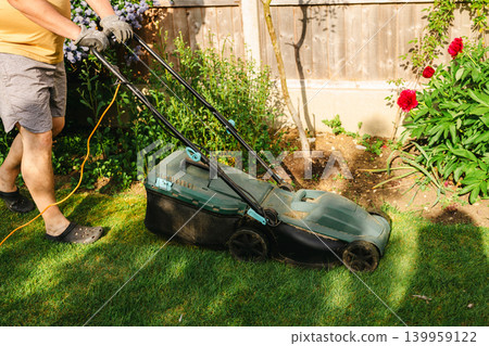 Person mowing lawn in backyard garden, home lawn care and summer yard maintenance Person mowing lawn in backyard garden, home lawn care and summer yard maintenance 139959122