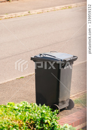 Black wheelie bin placed on residential street pavement for household waste collection Black wheelie bin placed on residential street pavement for household waste collection 139959152