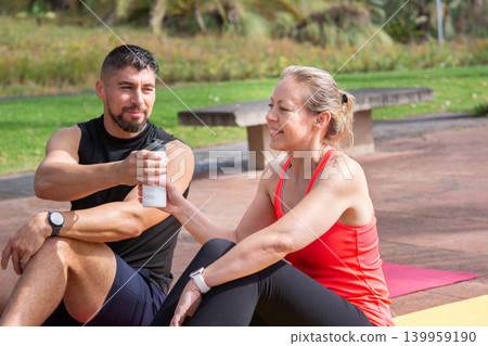 Two Friends Sharing Water During Outdoor Fitness Workout 139959190