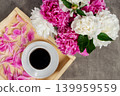 Flat lay of a white cup of black coffee on a wooden tray with pink flower petals next to a bouquet of peonies. Top view. 139959559