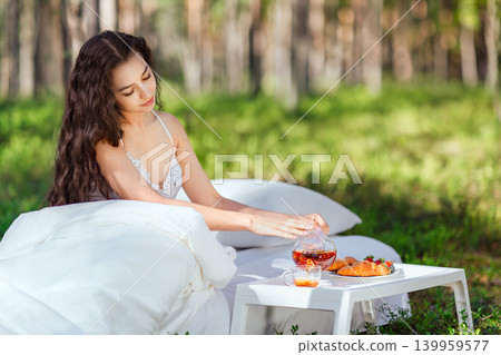 Young woman has breakfast in bed in a summer forest Young woman has breakfast in bed in a summer forest 139959577