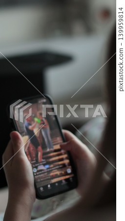 Vertical video. Close up shot of kid girl, surfing Internet and scrolling social networks using her mobile phone. Lifestyle concept. Vertical video. Close up shot of kid girl, surfing Internet and scrolling social networks using her mobile phone. Lifestyle concept. 139959814