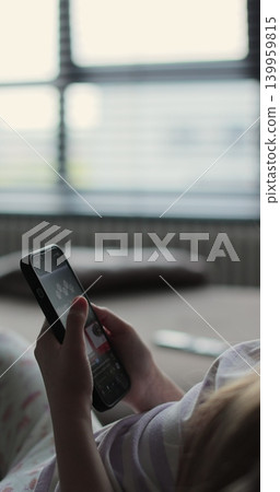 Vertical video. Close up shot of kid girl, surfing Internet and scrolling social networks using her mobile phone. Lifestyle concept. Vertical video. Close up shot of kid girl, surfing Internet and scrolling social networks using her mobile phone. Lifestyle concept. 139959815
