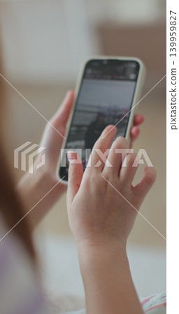 Vertical video. Little girl watching news feed social media smartphone message sitting cozy couch. Digital lifestyle. Vertical video. Little girl watching news feed social media smartphone message sitting cozy couch. Digital lifestyle. 139959827
