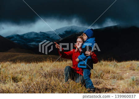 Mother and son looking out into the mountains in dark stormy weather Mother and son looking out into the mountains in dark stormy weather 139960037