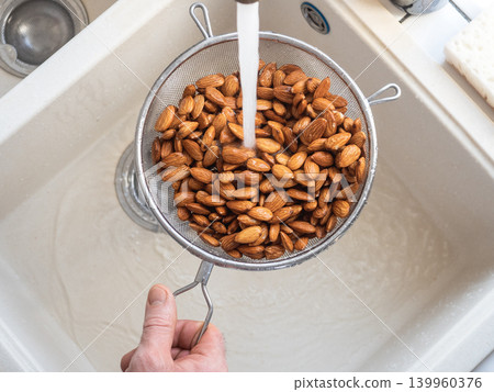 Man washes almonds in a metal colander 139960376