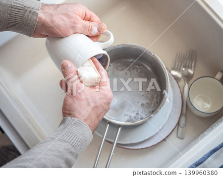 Man washes dishes in a kitchen sink Man washes dishes in a kitchen sink 139960380
