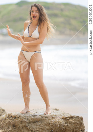Woman stands on rock by the sea and enjoys the water on a sunny day at the beach in summer season Woman stands on rock by the sea and enjoys the water on a sunny day at the beach in summer season 139961001