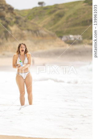 Woman stands in ocean waves and reacts to the water at a beach on a sunny day Woman stands in ocean waves and reacts to the water at a beach on a sunny day 139961035