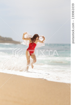 Woman in red swimsuit plays by the ocean shore during day at the beach in summer Woman in red swimsuit plays by the ocean shore during day at the beach in summer 139961039