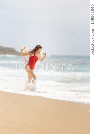 Woman in red swimsuit plays in the ocean waves at the beach on a sunny day during summer 139961040