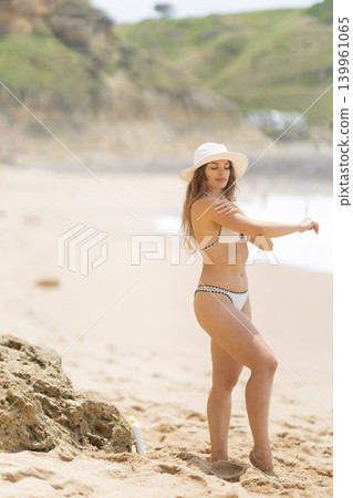 Woman applying sunscreen on beach in summer with clear sky and waves in background Woman applying sunscreen on beach in summer with clear sky and waves in background 139961065