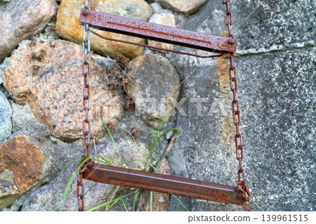 A rusty metal chain ladder hanging on a stone wall A rusty metal chain ladder hanging on a stone wall 139961515