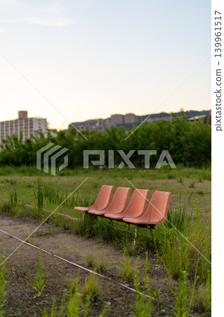 An orange bench left in a vacant lot covered with grass. An orange bench left in a vacant lot covered with grass. 139961517