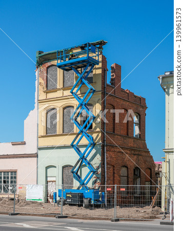 Blue scissor lift beside partially demolished historic brick building during urban redevelopment Blue scissor lift beside partially demolished historic brick building during urban redevelopment 139961573