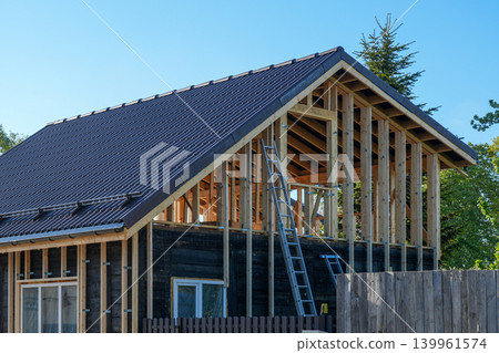 Wooden frame house under reconstruction with roof tiles and exposed timber structure framing work 139961574