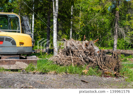 Excavator clearing tree stumps and roots from forest land for construction site preparation Excavator clearing tree stumps and roots from forest land for construction site preparation 139961576