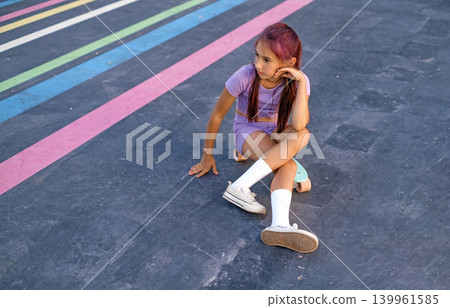 A teenage girl in a purple T-shirt is sitting on a skateboard, thoughtfully looking away. A teenage girl in a purple T-shirt is sitting on a skateboard, thoughtfully looking away. 139961585